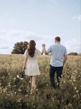 Couple walking hand in hand through a summer meadow, seen from behind