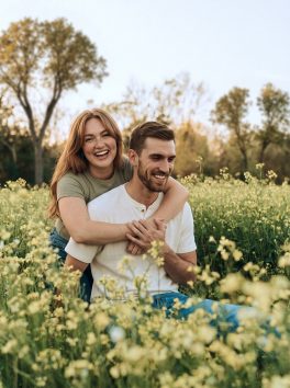 Couple laughing together among tall yellow canola flowers