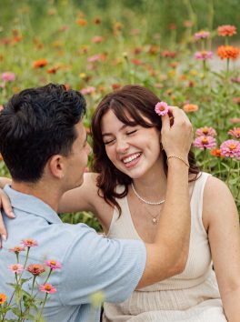 One partner tucking a flower behind the other’s ear in a flower field